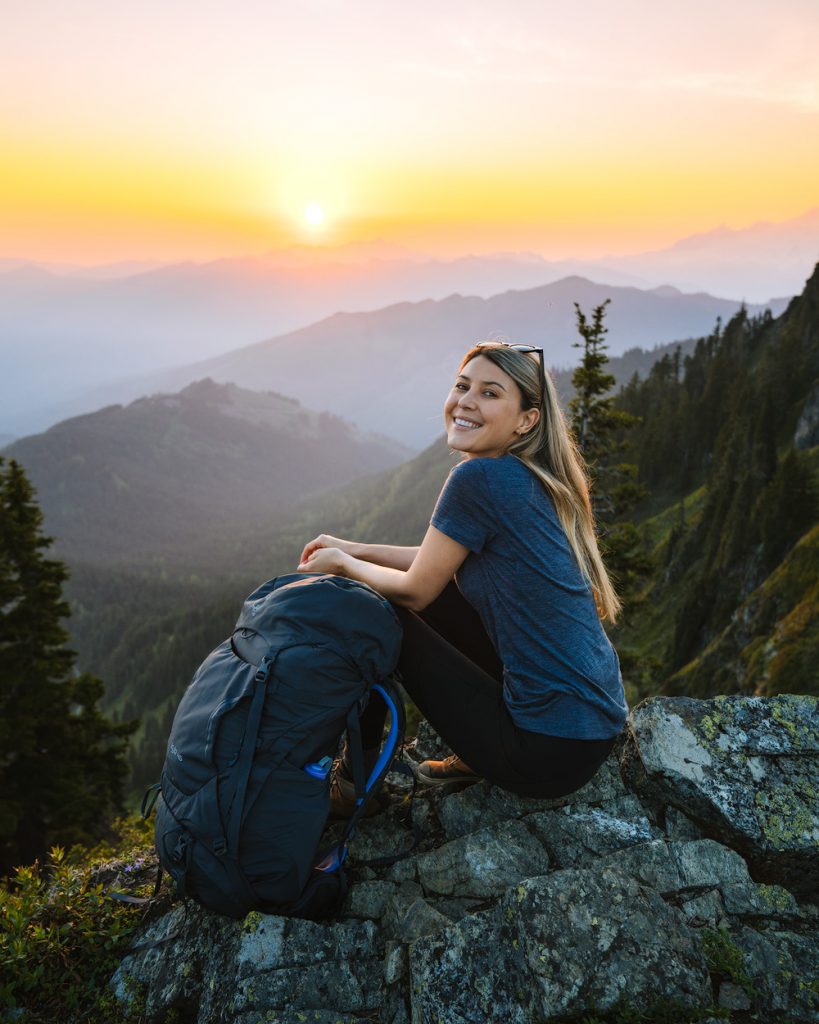 Young person hiking female sitting on top rock, Backpack woman